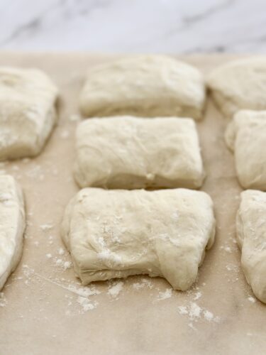 Eight pieces of uncooked dough resting on parchment paper, with a dusting of flour.
