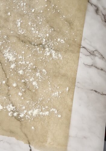Baking parchment paper with flour dust scattered on a marble countertop.