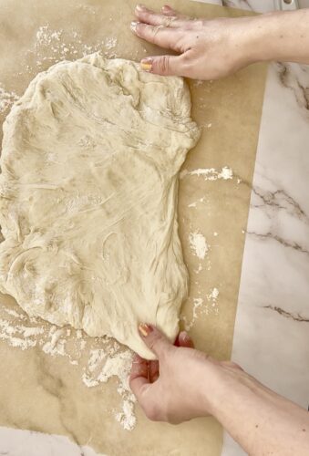 Hands stretching pizza dough on parchment paper