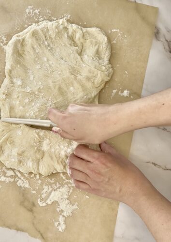 Close-up of hands cutting dough on a floured surface with a knife.