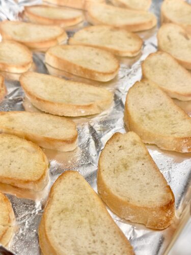 Golden brown slices of toasted bread arranged on a sheet of aluminum foil.