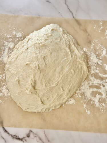 A ball of dough resting on a floured surface, surrounded by scattered flour.