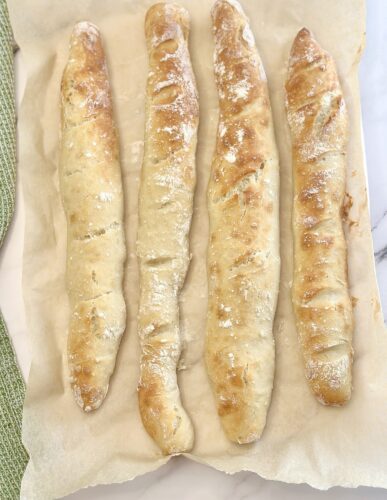 Four freshly baked breadsticks arranged on parchment paper.