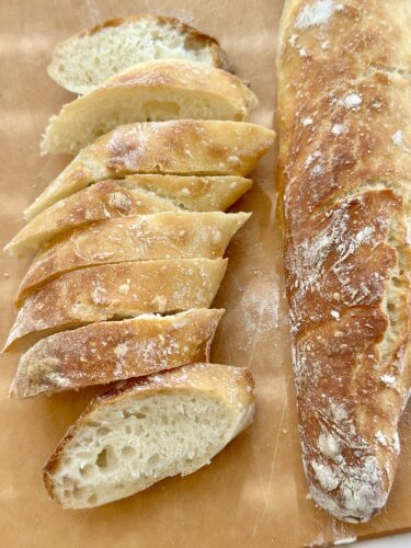 A freshly baked loaf of bread sliced into even pieces, with a crusty exterior and soft interior, placed on a wooden board.