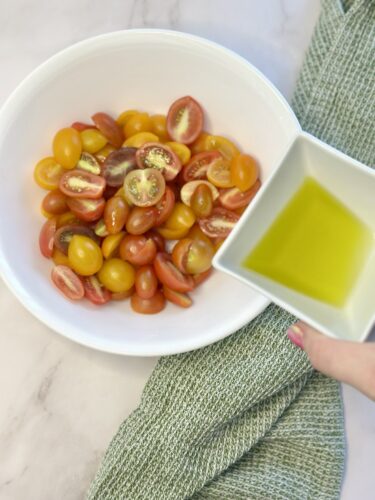 A bowl of mixed cherry tomatoes, including red and yellow varieties, with a small dish of olive oil held beside it.