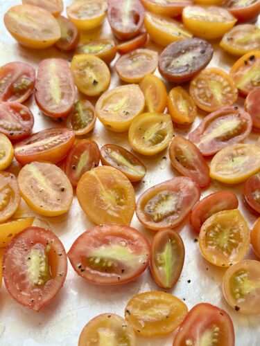 A close-up image of halved cherry tomatoes in various colors, including red, yellow, and orange, scattered on a surface.