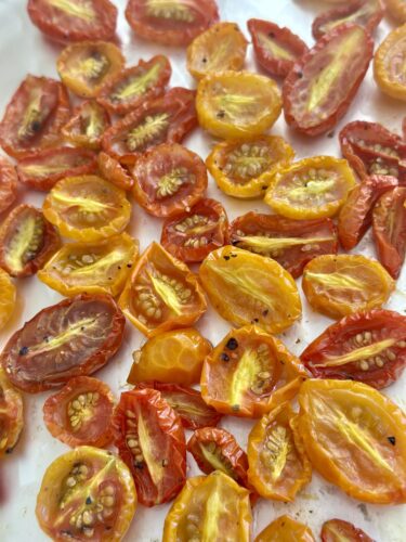 A close-up of sliced, roasted tomatoes in various shades of red and yellow, spread out on a white surface.