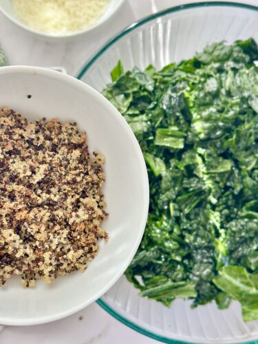 A bowl of cooked quinoa next to a large bowl of fresh chopped greens, with additional ingredients visible in the background.