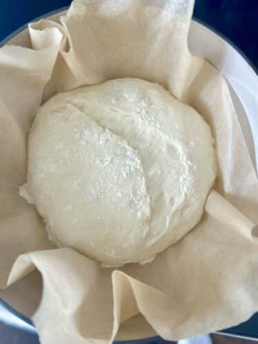 A ball of dough resting in a bowl lined with parchment paper.