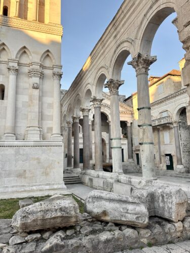 Historical ruins featuring stone arches and columns, with remnants of ancient structures in the foreground.