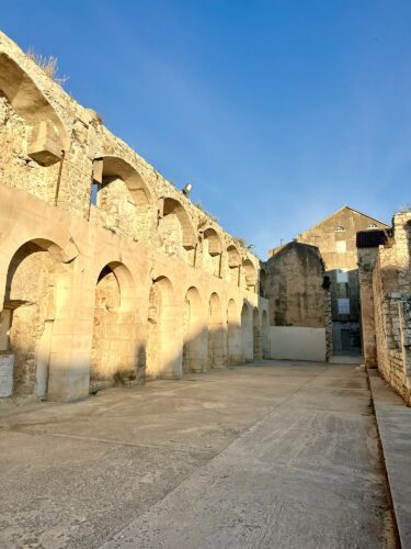 Ruins of an old stone building with arched windows and walls under a clear blue sky.