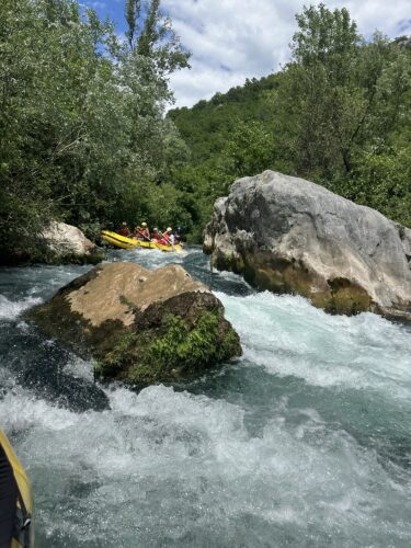 A group of people in yellow rafts navigating through a rocky, fast-flowing river surrounded by lush greenery.