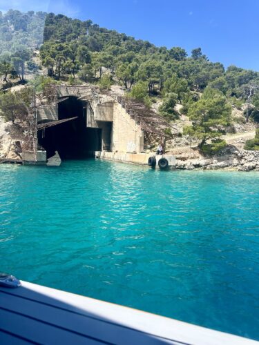 A picturesque view of a turquoise body of water with a rocky shoreline and a natural cave entrance, surrounded by lush greenery and trees.