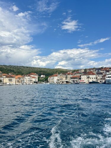 Scenic view of a coastal town with multi-colored buildings along the shore, under a partly cloudy sky and blue waters.