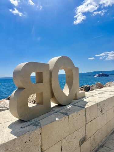 A large stone sculpture displaying the number '108', placed on a stone wall with a view of the blue sea and cloudy sky in the background.