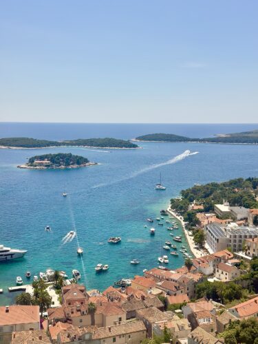 Aerial view of a coastal landscape featuring blue waters, small islands, and boats anchored along the shore with a backdrop of a clear sky.