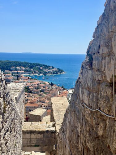 View of a coastal town from a stone pathway, with the sea and islands in the background