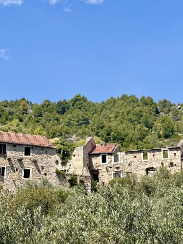 Ruins of an old stone building set against a green hillside under a blue sky.