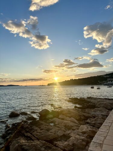 Scenic view of a sunset over the sea with rocky shoreline and boats in the distance.