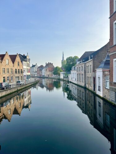 Scenic view of a canal in a historic town, with charming buildings lining both sides and reflections in the water, under a clear blue sky.