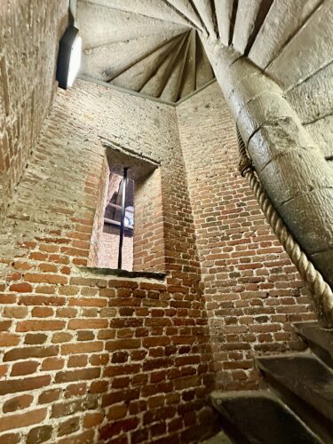 Interior view of a spiral staircase with exposed brick walls and a small window.