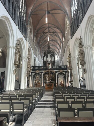 Interior view of a church featuring rows of chairs, tall arched ceilings, intricate architectural details, and a central altar area.