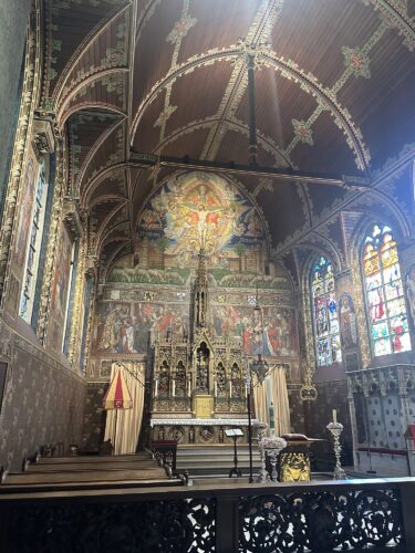 Interior view of a richly decorated chapel featuring intricate murals, a detailed altar, and stained glass windows.
