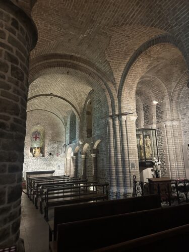 Interior view of a rustic church featuring arched stone ceilings, wooden pews, and decorative artwork.
