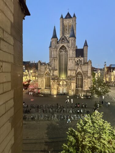 View of a historic church with tall spires during twilight, surrounded by a square filled with bicycles and trees.
