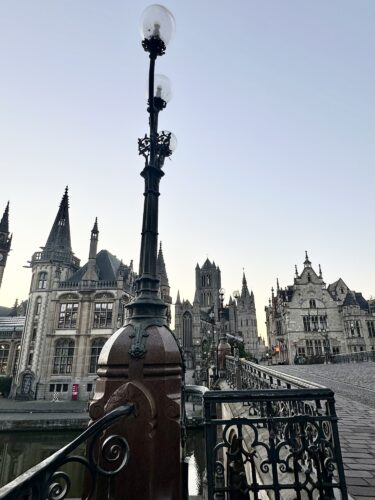 Historic buildings with ornate architecture alongside a river, featuring a decorative street lamp in the foreground.