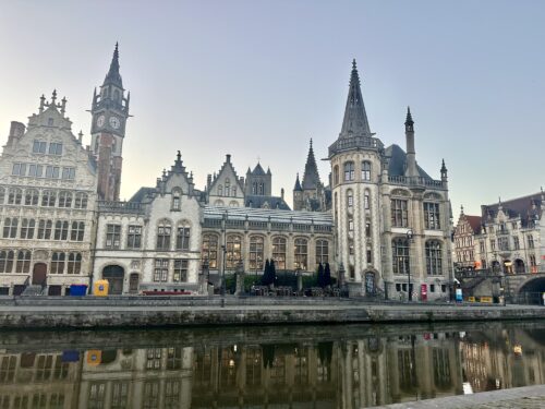 Historic buildings along a canal in Ghent, Belgium, featuring intricate architecture and a clear sky.