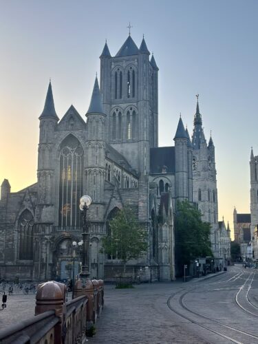 A historic stone church with tall spires and intricate architecture, located in an urban setting during sunrise.