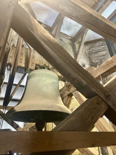 A close-up view of a large bell hanging within a wooden frame, showcasing the bell's details and the surrounding structure.
