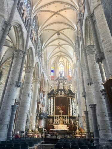 Interior view of a grand church featuring tall stone columns, vaulted ceilings, and a decorative altar with an ornate backdrop.