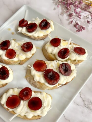 A plate of small bread slices topped with creamy white frosting, shredded coconut, and bright red cherry slices.