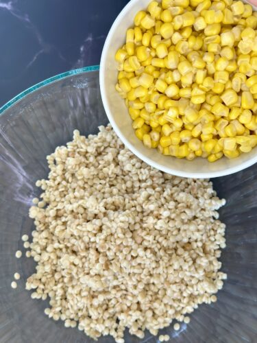A glass bowl with a heap of cooked quinoa and a white bowl filled with yellow corn kernels placed above it.