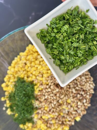 Chopped green herbs being added to a bowl of corn and grains.