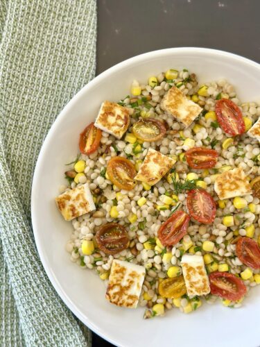 A vibrant salad featuring pearl barley, cherry tomatoes, corn, and fresh dill, topped with golden-brown pieces of grilled cheese.