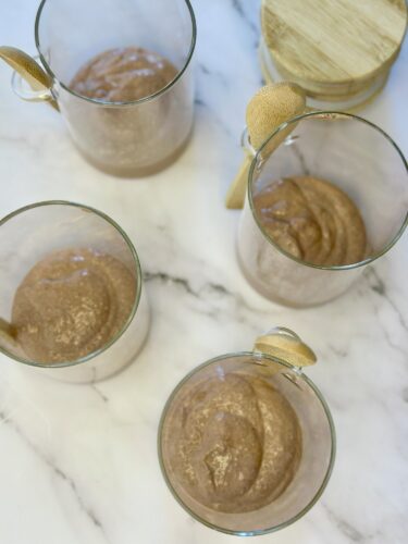 Four glass cups filled with chocolate mousse, each topped with a spoon, on a marble surface.