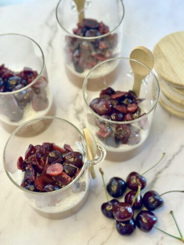Bowls of dessert topped with cherries and wooden spoons, placed on a marble surface.