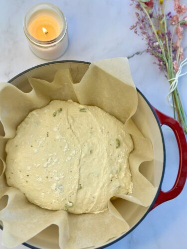 A bowl of dough rising in parchment paper, surrounded by a lit candle and dried flowers.