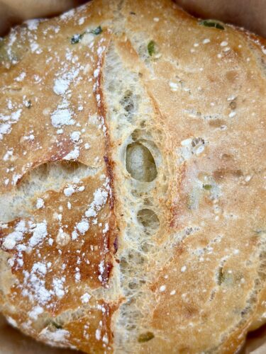 Close-up of a crusty bread roll with visible air pockets and sprinkled flour on top.