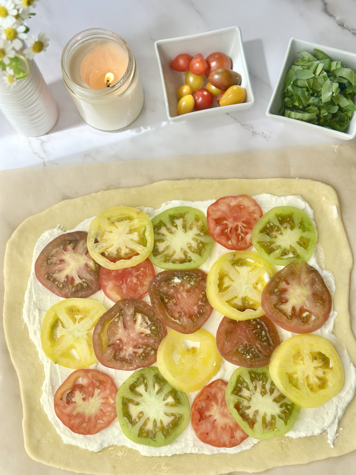 Unbaked pastry topped with cream cheese and colorful sliced tomatoes, with basil and cherry tomatoes nearby