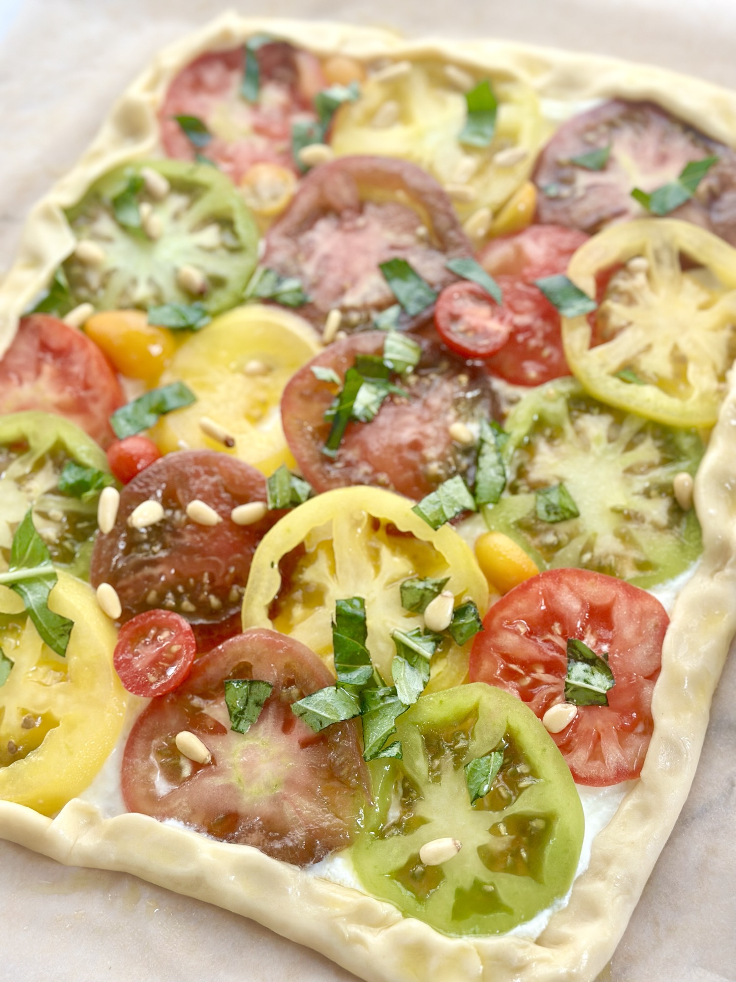 Rustic tart topped with multicolored heirloom tomatoes, basil, and pine nuts