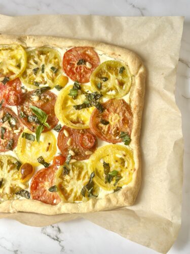 Close up slice of heirloom tomato puff pastry tart showing layers of feta, tomato, and basil
