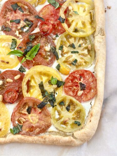Heirloom tomato puff pastry tart topped with whipped feta, sliced tomatoes, basil, and pine nuts