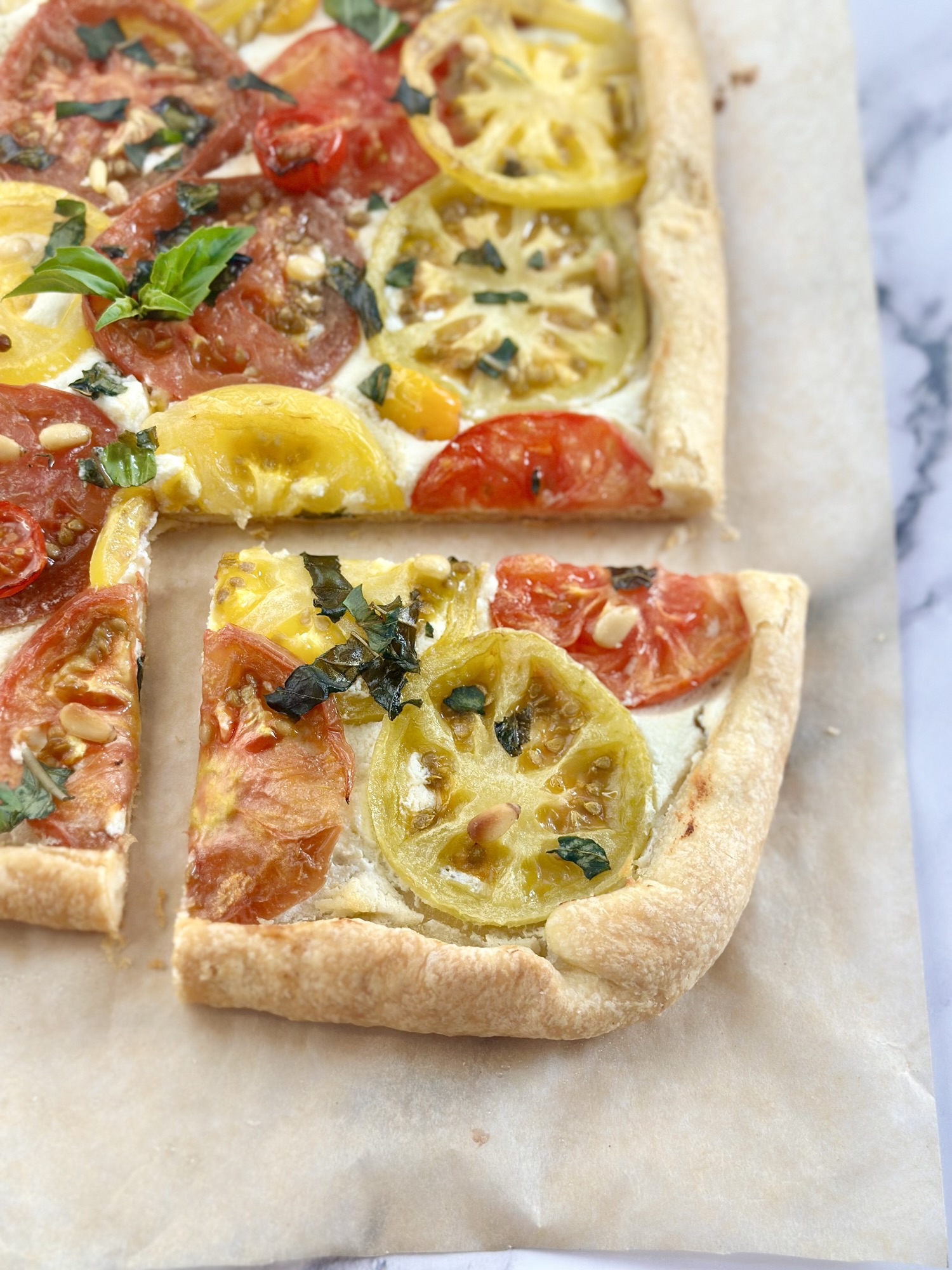 Sliced tomato tart with red and yellow tomatoes, basil, and pine nuts